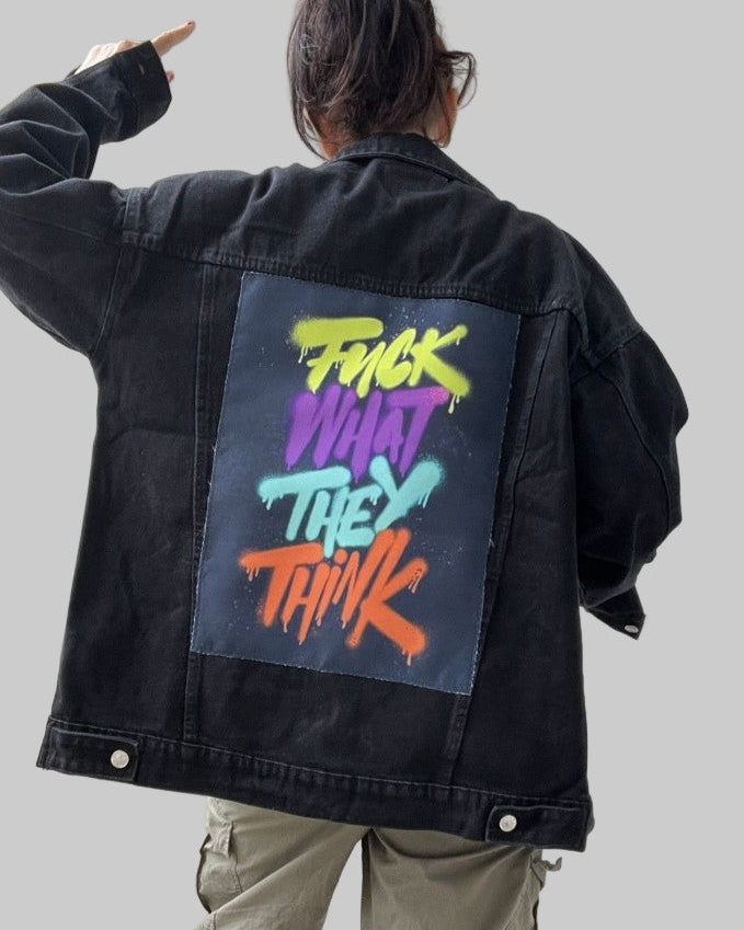 Person wearing a black jacket with colorful text on the back, standing in front of a white door.