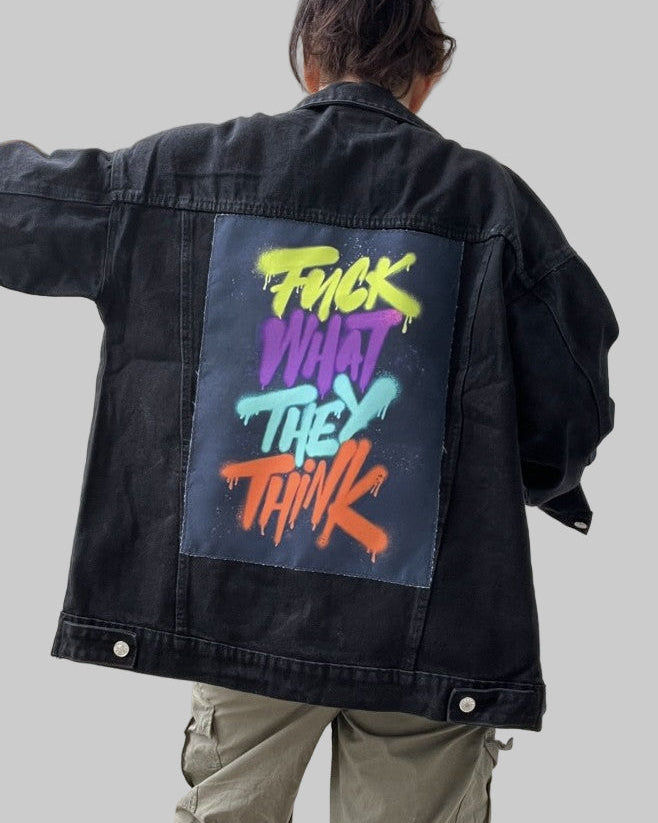 Person wearing a black jacket with colorful text on the back, standing in a neutral setting.
