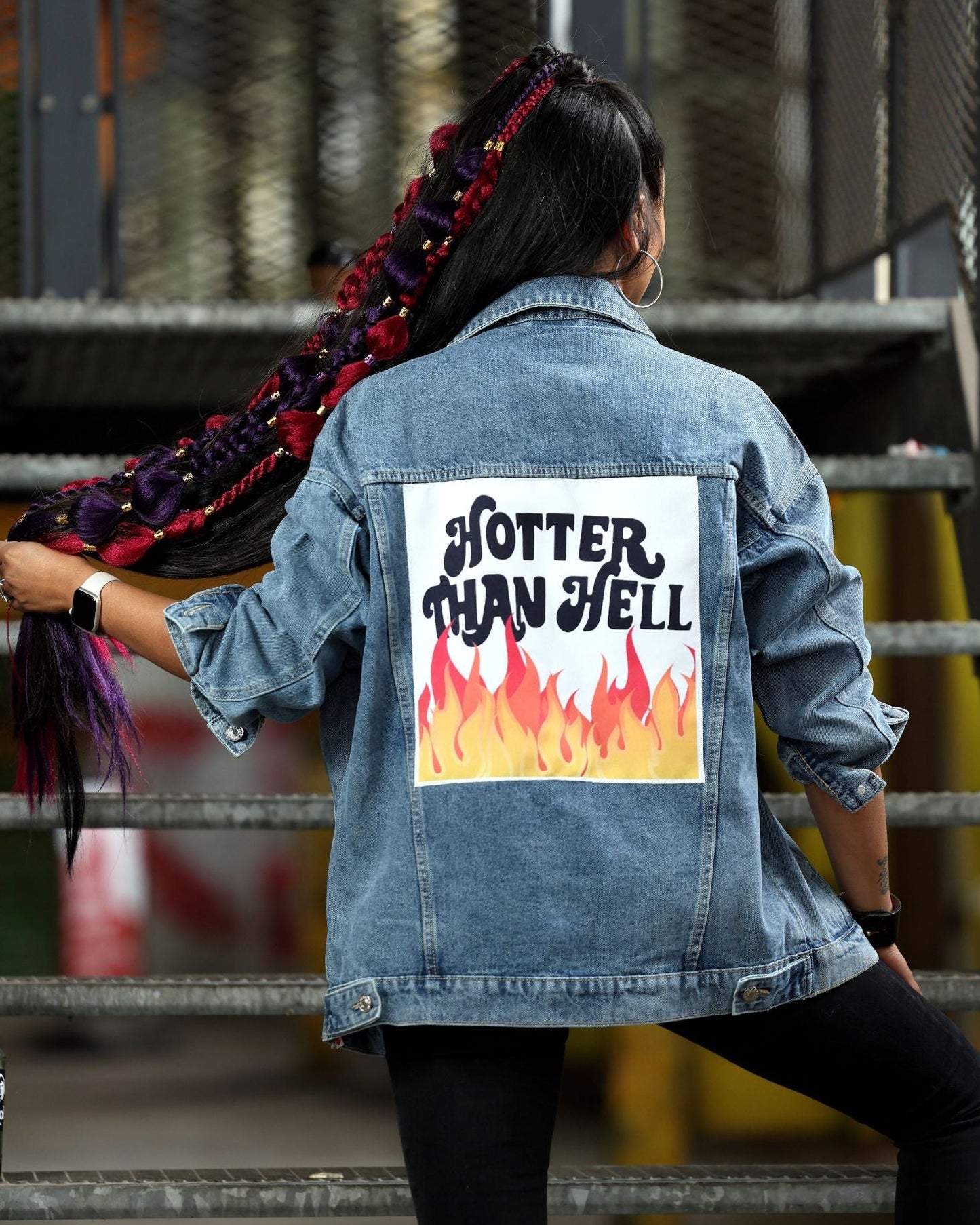 Person wearing a denim jacket with 'Hotter Than Hell' graphic on the back, standing in an industrial setting.