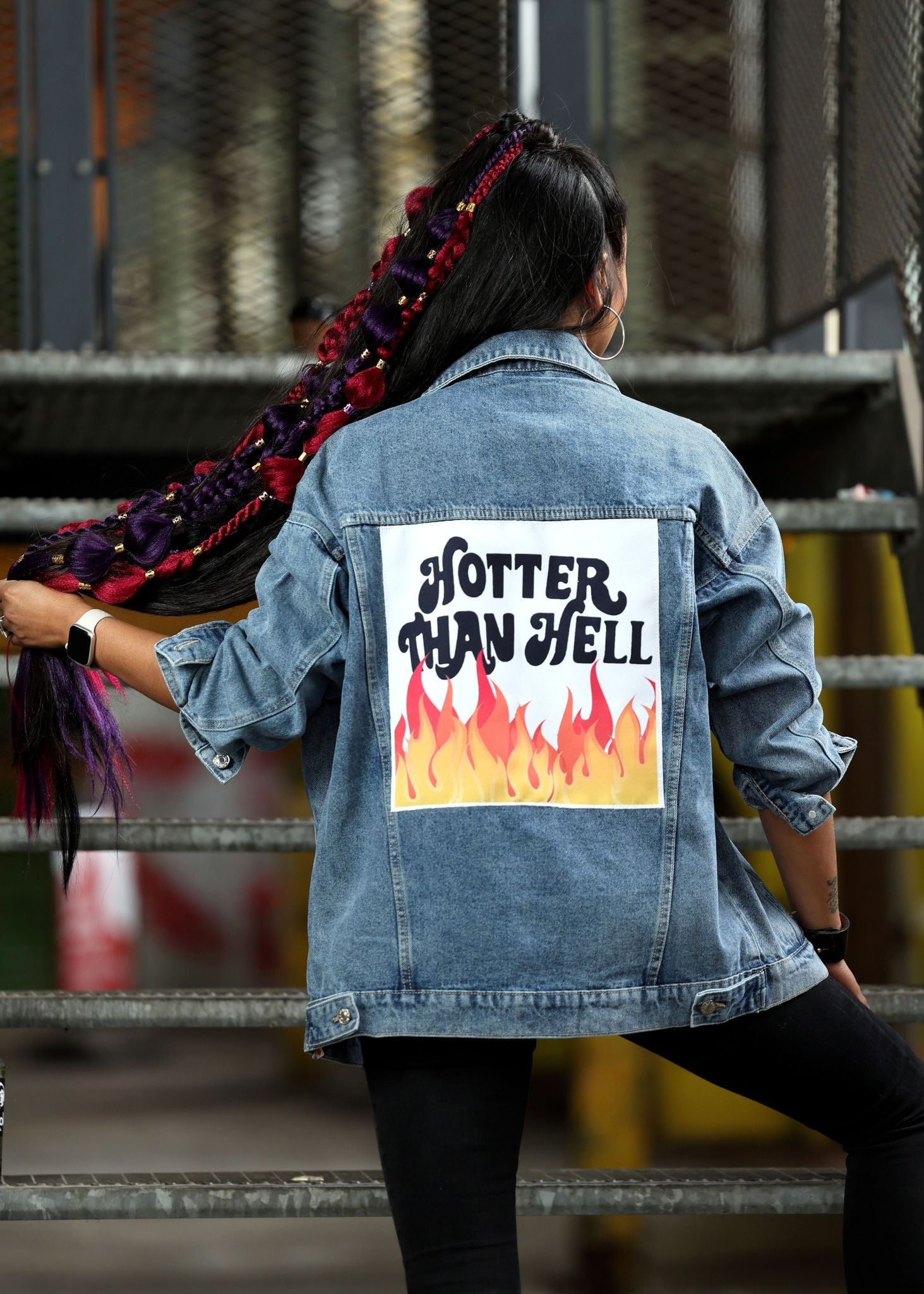 Person wearing a denim jacket with 'Hotter Than Hell' graphic on the back, standing in an industrial setting.