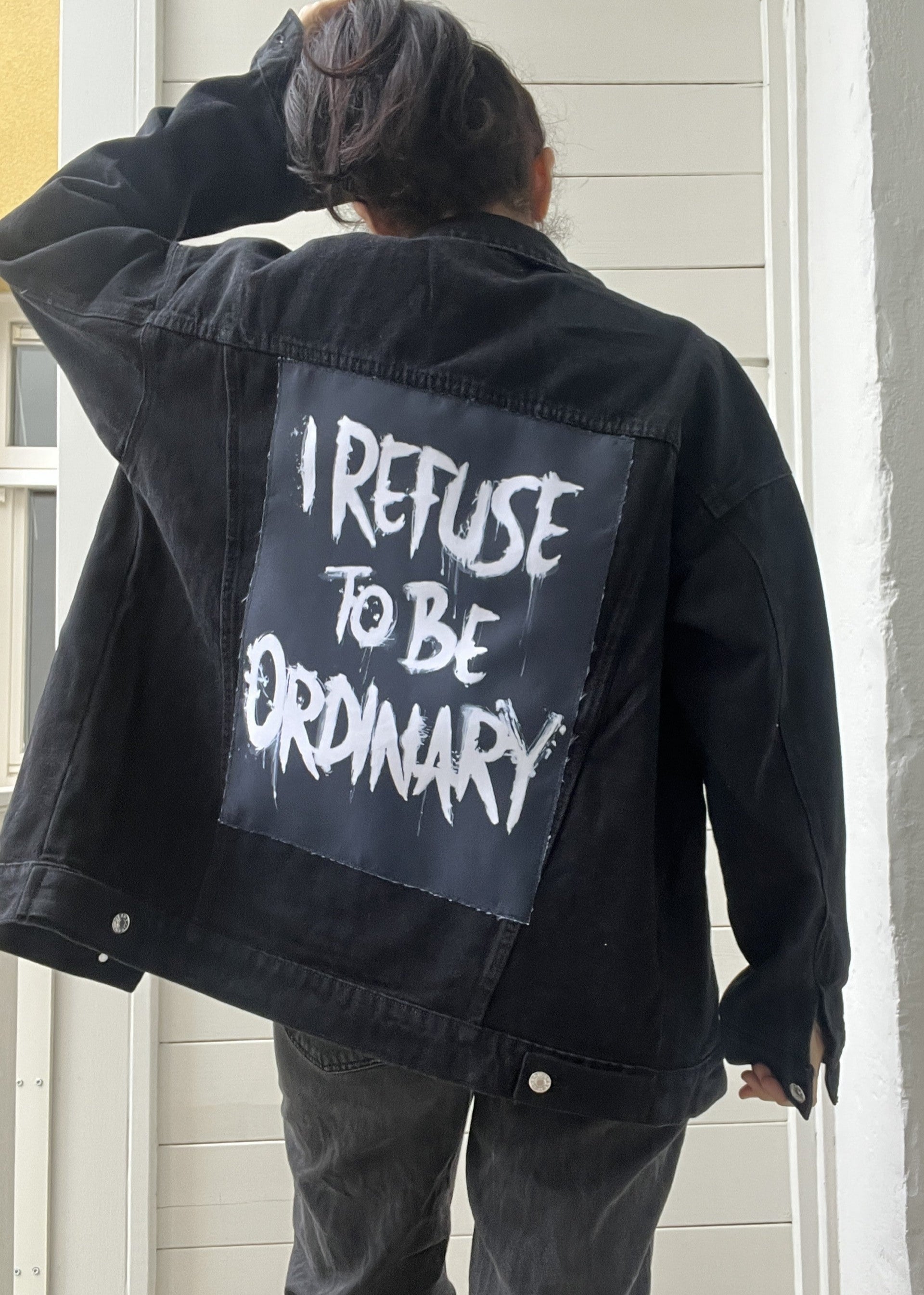 Person wearing a black jacket with 'I Refuse to be Ordinary' text on the back.