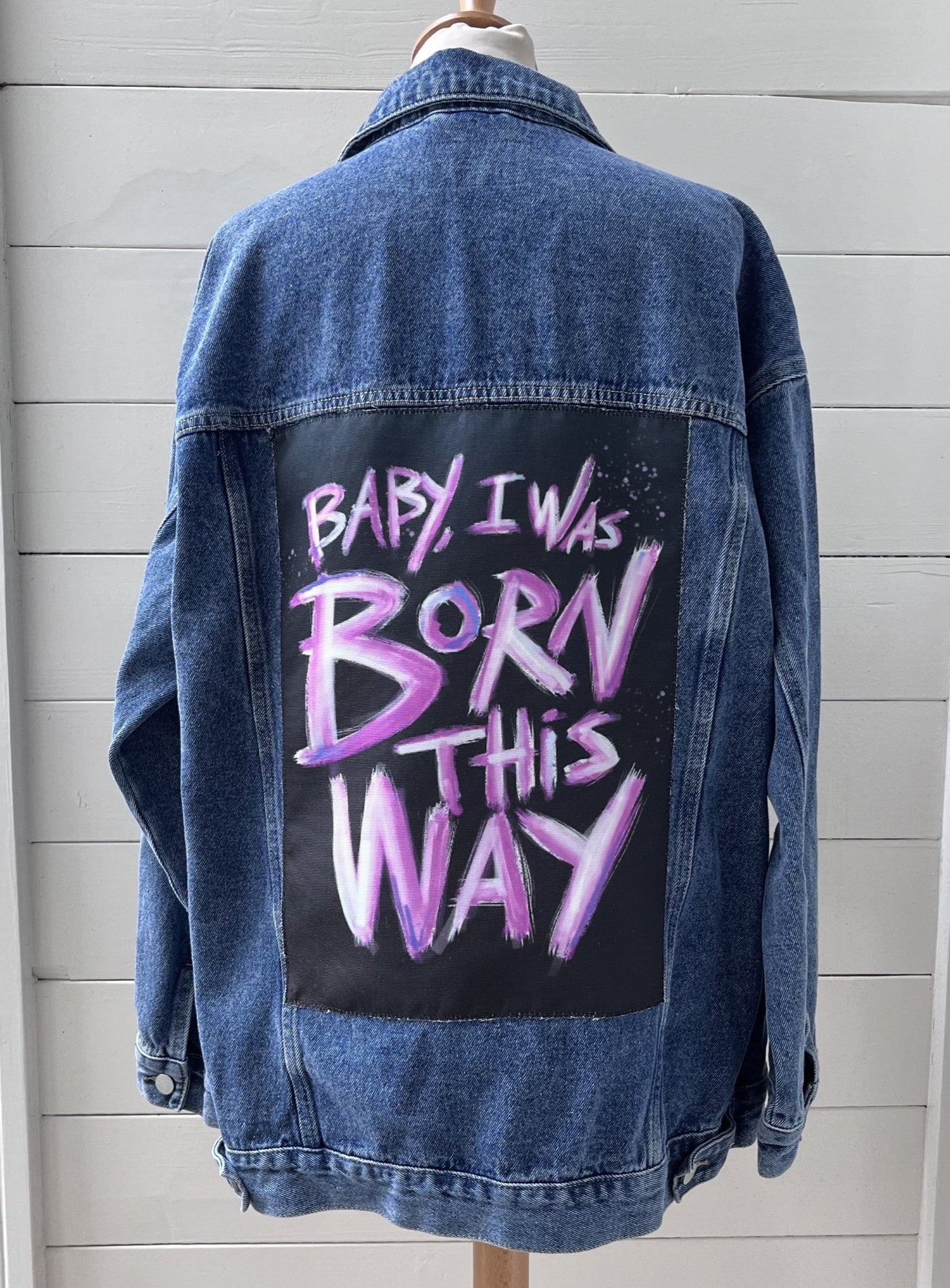 Denim jacket with 'Baby I was born this way' text on a mannequin against a light gray background