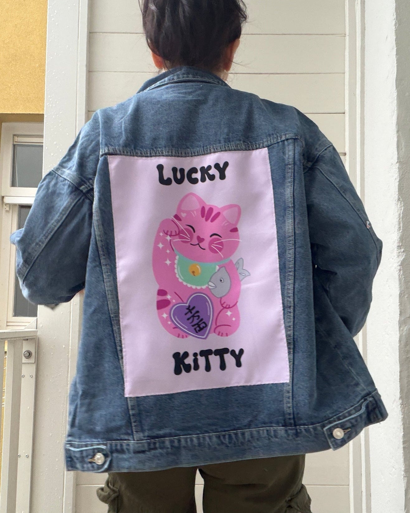 Person wearing a denim jacket with a 'Lucky Kitty' design on the back.