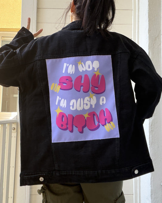 Person wearing a black jacket with colorful text on the back, standing in front of a white door.