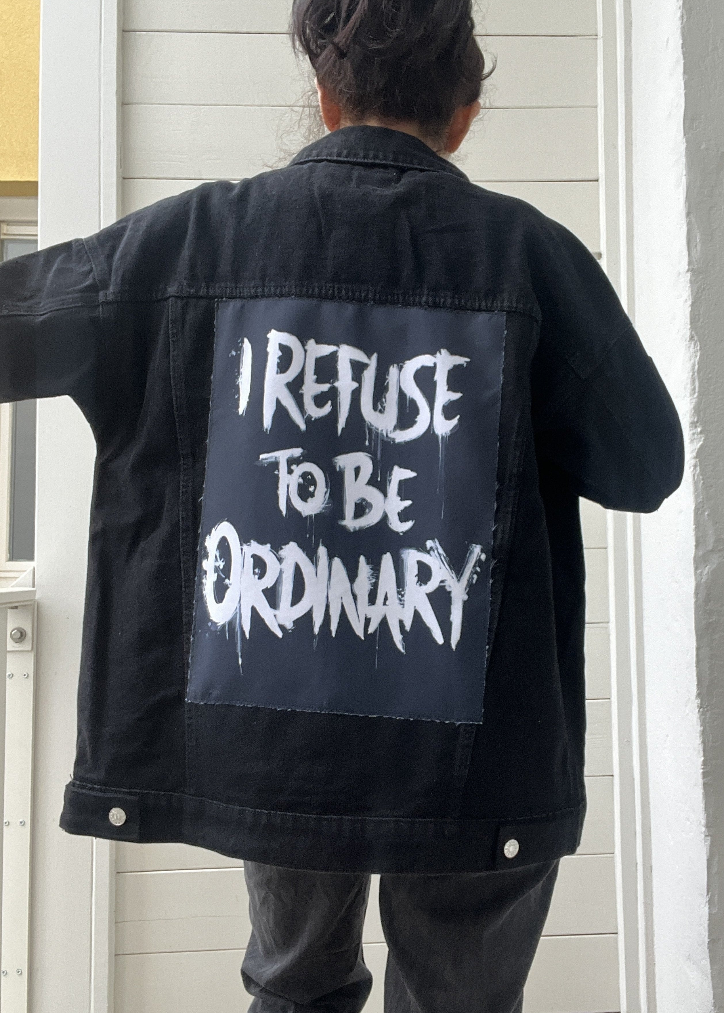 Person wearing a black jacket with 'I Refuse to be Ordinary' text on the back.
